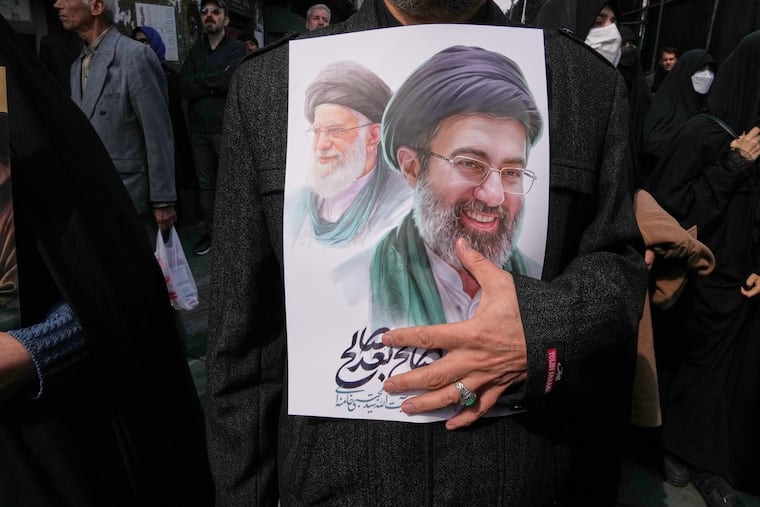 A mourner holds a poster depicting Ayatollah Mojtaba Khamenei, right, the successor to his late father Ayatollah Ali Khamenei, left, as supreme leader, during the funeral procession for senior Iranian military officials and civilians killed during the U.S.-Israel campaign in Tehran, Iran, Wednesday, March 11, 2026.