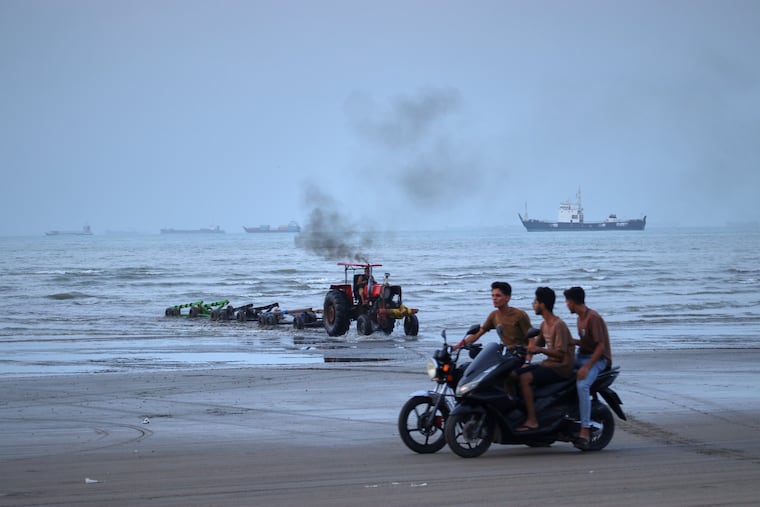 Young men ride motorcycles along the shore as a tractor pulls equipment from the water and commercial vessels appear anchored in the Strait of Hormuz off Bandar Abbas, Iran, Monday, July 27, 2026.