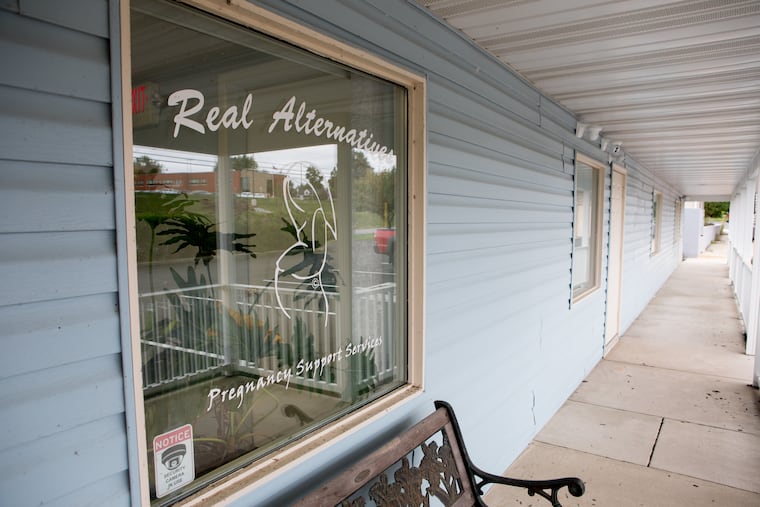 Real Alternatives, an anti-abortion organization that's received more than $100 million from the state of Pennsylvania, sits in an office plaza Harrisburg, near a thrift store and a pizza shop and across from an elementary school, visible in the reflection.