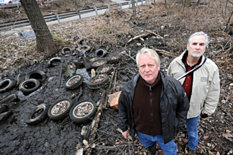 GOAL president Dale Frazier (left) and board member Ed Armstrong stand next to discarded tires at a Levittown site. Frazier estimates that the organization has removed 35 tons of debris, 700 tires. (Clem Murray / Staff Photographer)