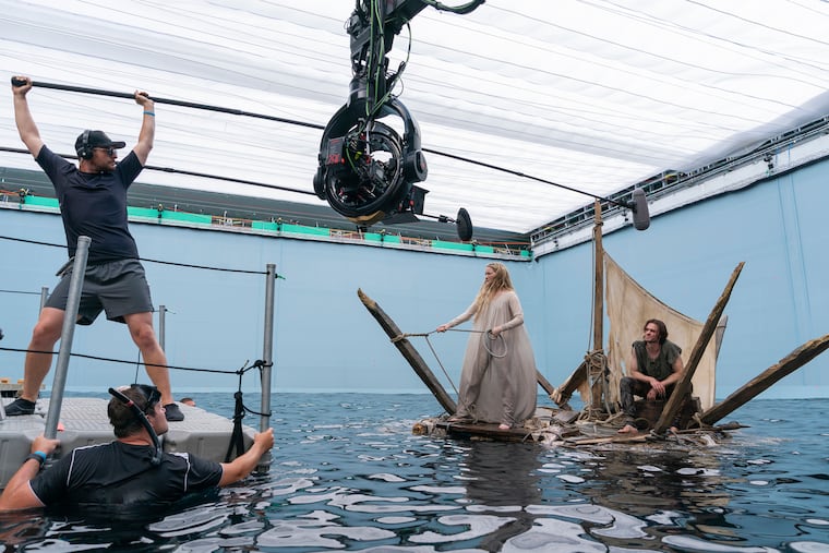 This image released by Amazon Studios shows Morfydd Clark, center, and Charlie Vickers, right, on the set of "The Lord of the Rings: The Rings of Power."