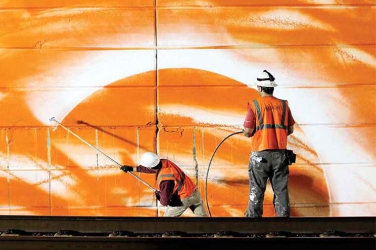 Mural Arts Project artist Tom Walton (left) sprays paint on the walls as Staff Artist Nathaniel Lee assist, along Amtrak Northeast Corridor route, near 30th Street Station on Sunday, May 11, 2014. ( Yong Kim / Staff Photographer )
