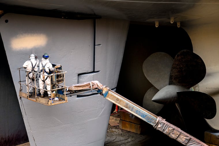 Workers paint a rudder, near the stern and propellers of the Battleship New Jersey.