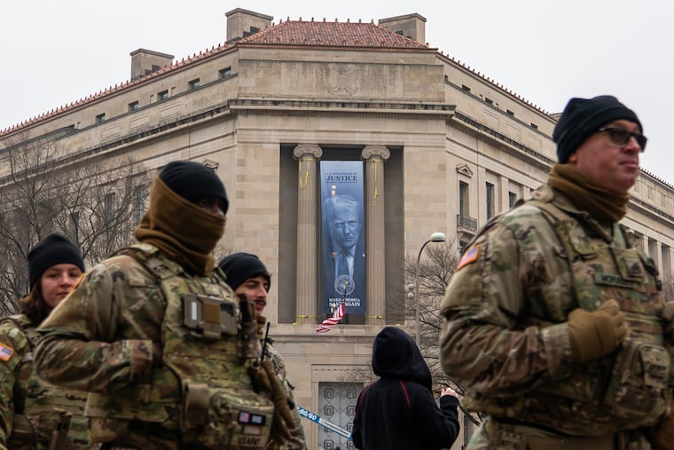 Members of the National Guard walk past a banner with President Donald Trump hanging on the Department of Justice on Thursday.