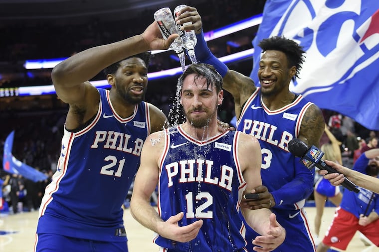 T.J. McConnell getting doused with water by teammates Robert Covington (right) and Joel Embiid at the end of Monday night’s game.