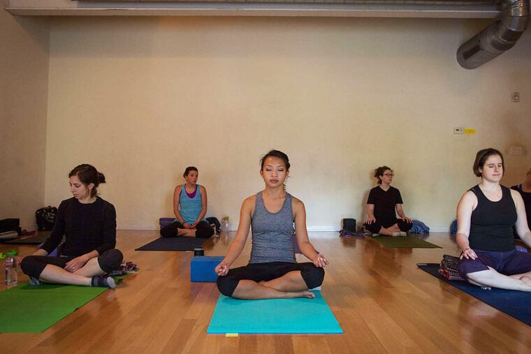 Students prepare for class at Studio 34 Yoga in West Phila., some with "consent" cards on their mats. Instructors link the trend to greater awareness of yoga injuries and trauma from assaults.