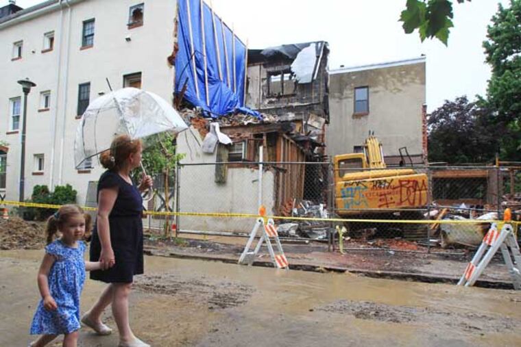 In early May, the residents of the 2300 block of Naudain Street in Philadelphia were awaken by shrieking carbon monoxide detectors. Officials from the Fire Department and Philadelphia Gas Works responded and measured off-the-charts levels of the poisonous gas. A few minutes later, a rowhouse exploded, taking down the neighboring structures as well. Laura Brennan and her daughter, Sara Brennan, 3, walk by the ruins on June 19, 2014. ( CHARLES FOX / Staff Photographer )