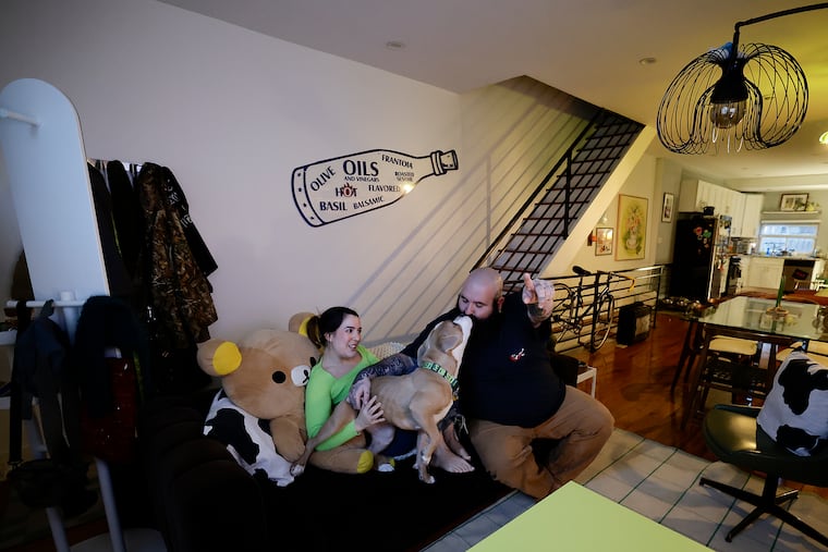 Sam Gellerstein gets a kiss from dog, Mooshy, as girlfriend Sara Sarmiento looks on in their South Philadelphia home on Friday, Feb. 27, 2026.