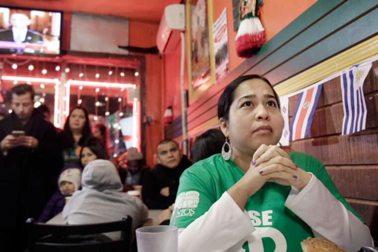 Belinda Holguin clasps her hands and listens to President Obama's immigration address at Taquitos de Puebla in South Philadelphia on November 20, 2014. ( ELIZABETH ROBERTSON / Staff Photographer )