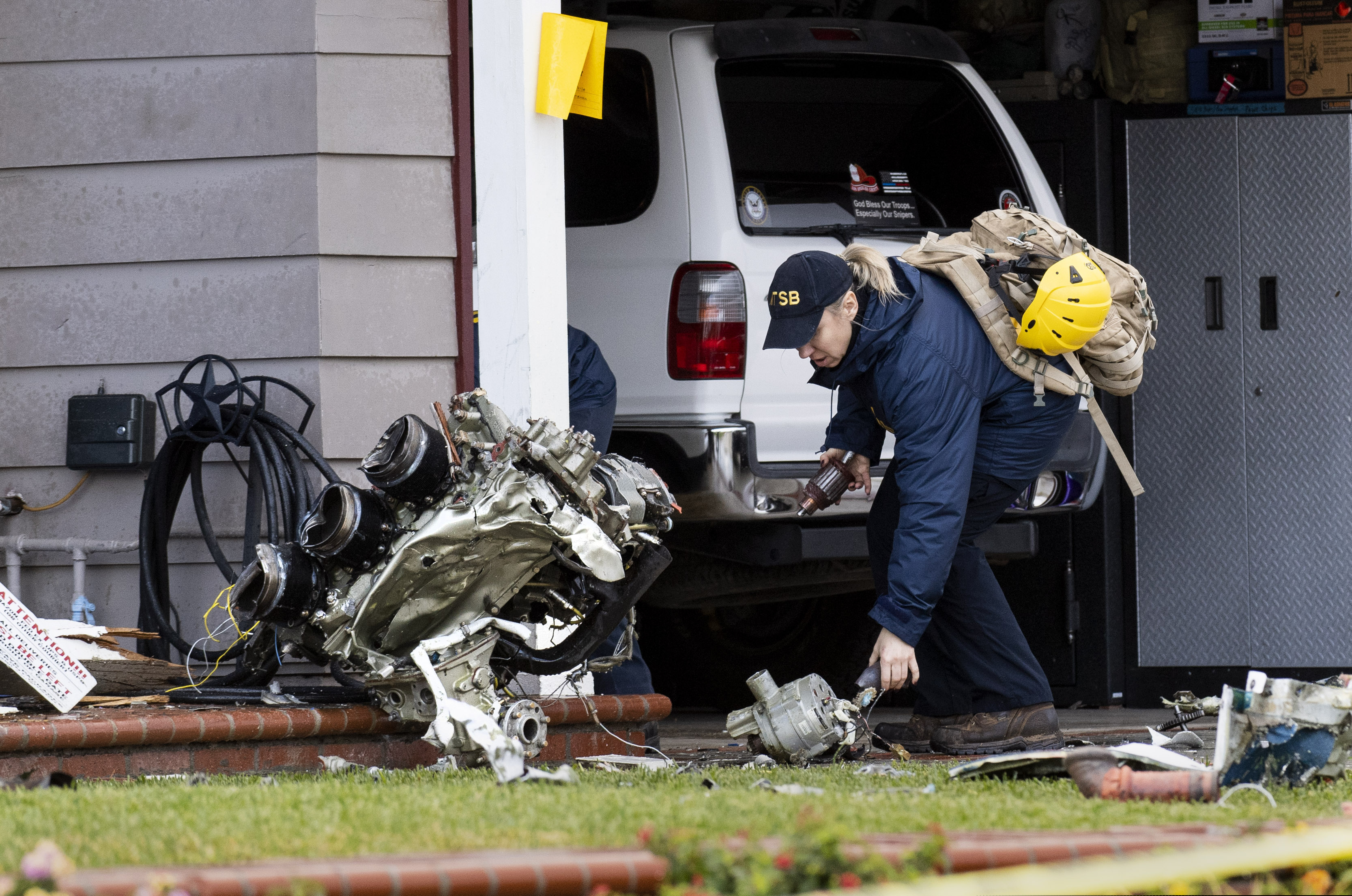 A National Transportation Safety Board worker takes a photo of an engine that came to rest against a house on Crestknoll Drive in Yorba Linda, Calif., on Monday, Feb. 4, 2019. The debris field from a small plane crash a day earlier covered several blocks with one home catching fire. The pilot and four people on the ground died. (Paul Bersebach / Orange County Register via AP)