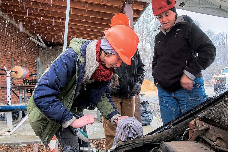 Volunteer Emily Southern checks the oil on a "mini steers" machine as trainer Valerie Naylor, right, looks on.