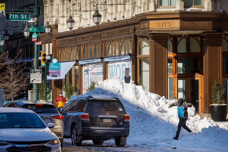 An Amazon delivery driver rushes back to a car parked near a giant pile of snow at Seventh and Market Streets on Tuesday.