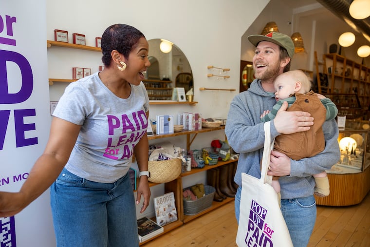 Fleche Jones, of Atlanta, Ga., Event Staff for Paid Leave for All, is showing James Taylor, of Medford Lakes, N.J., and his son Wilson, 10-months-old, on some of the free baby gifts during the Pop-up for Paid Leave at Moon + Arrow in Philadelphia, Pa., on Saturday, May 10, 2025.