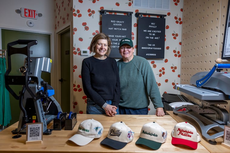 Valerie Safran (left) and Marcie Turney (right), pose behind the hat patch bar at Red Gravy Goods, the gift shop the couple opened on Dec. 9, 2025, at 1335 Passyunk Ave.