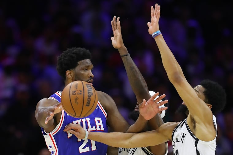 Sixers center Joel Embiid passes the basketball past Brooklyn Nets forward Royce O'Neale and guard Spencer Dinwiddie.