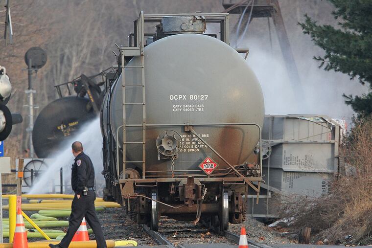 A Police officer walks by and takes a llok as water is being sprayed onto the tanker cars that were derailed in Paulsboro, NJ in 2012. ( MICHAEL BRYANT / Staff Photographer )