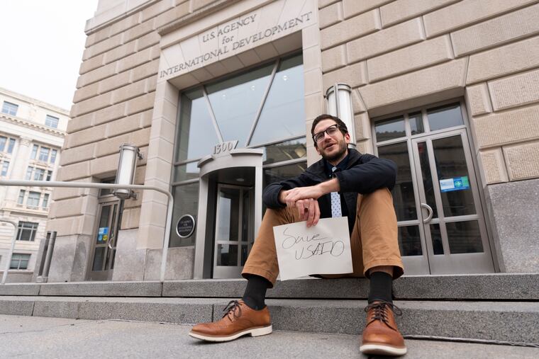 A United States Agency for International Development, or USAID, contract worker sits in front of the USAID office Monday in Washington with a message written on a piece of paper.