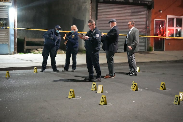 Police and homicide detectives investigate a double homicide at 60th and Delancy Streets on Monday. Three other people were injured, police said, after a masked gunman in a white vehicle opened fire into a crowd.
