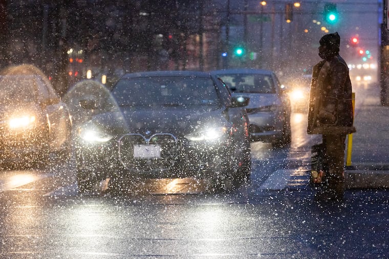 A pedestrian crosses North Broad Street at Cecil B. Moore Avenue as snow is illuminated in the headlights of traffic Friday. More is on the way through Monday, this time with expected accumulations of up to 4 inches.