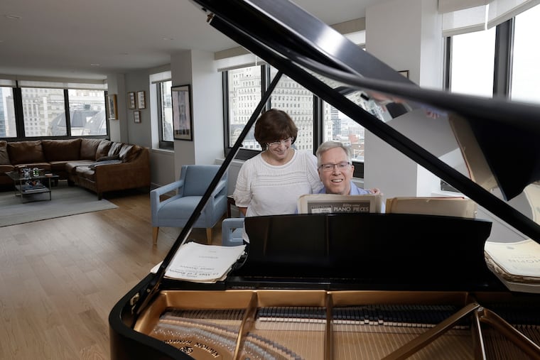 Mindy Hauptman looks on as her husband, Bill Hauptman, plays the Steinway piano in their newly renovated Academy House condo in Philadelphia.