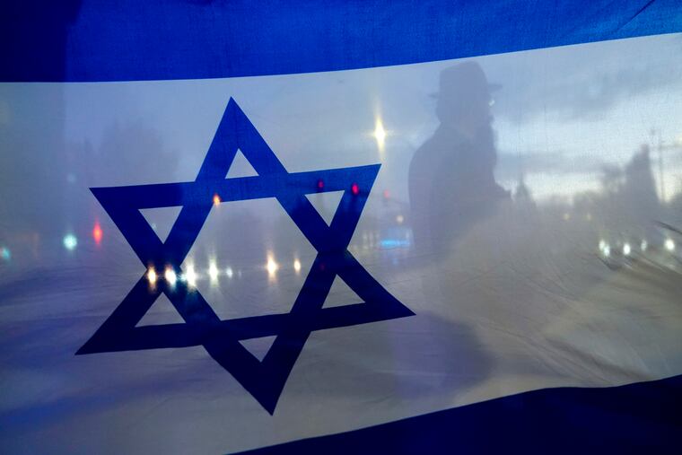 A demonstrator crossing the street is silhouetted behind the Israeli flag during a rally in support of Israel on Monday in Bellevue, Wash.