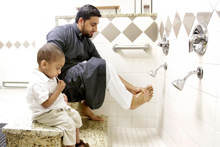 Maheen Khan washes his feet before the meal and prayer as his son, Ibrahim, sits with him. Khan is the organizer of the "iftar" at the Islamic Society of Greater Valley Forge. ELIZABETH ROBERTSON / Staff Photographer
