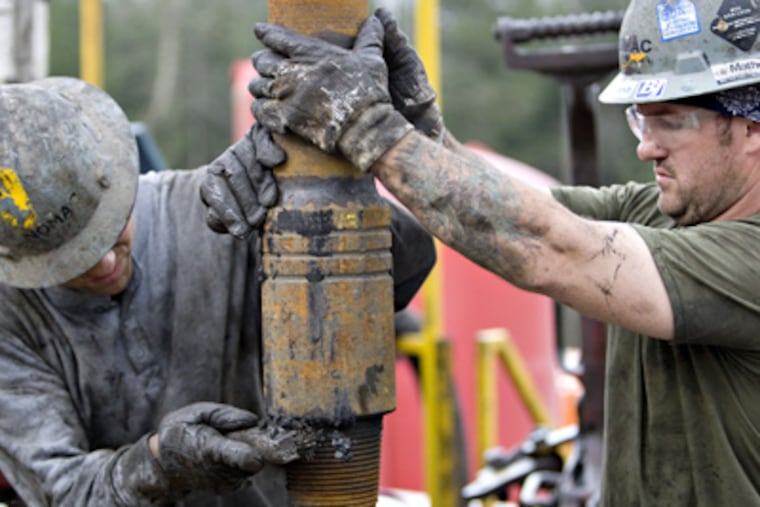 One worker steadies a section of pipe while another cleans the connection during shale-gas drilling operations. (Daniel Acker / Bloomberg)