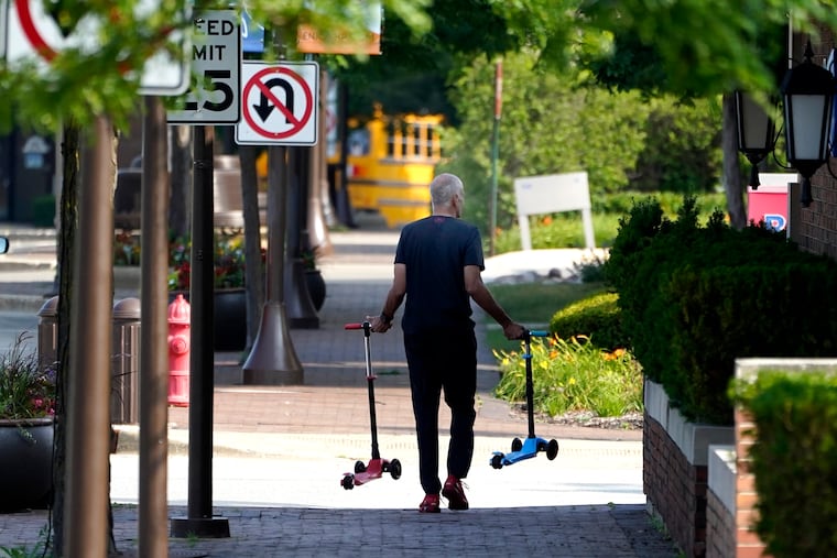 A man removes two children's scooters one day after a mass shooting in downtown Highland Park, Ill., Tuesday, July 5, 2022. A shooter fired on an Independence Day parade from a rooftop spraying the crowd with gunshots initially mistaken for fireworks before hundreds of panicked revelers of all ages fled in terror.