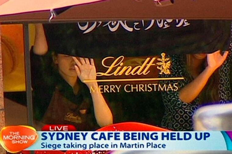 This image taken from live television in Sydney shows people holding up a black banner with Arabic writing on it inside the Lindt Chocolat Cafe Monday.