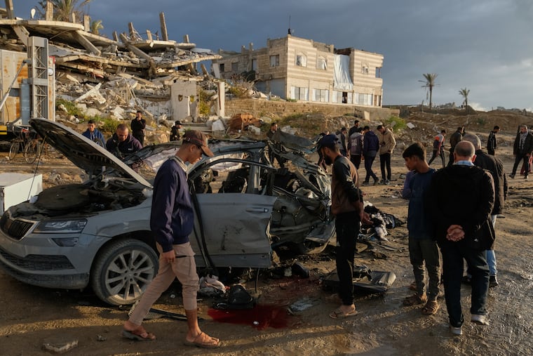 Palestinians looks at a destroyed car following an Israeli strike in Gaza City, Saturday, Dec. 13, 2025.