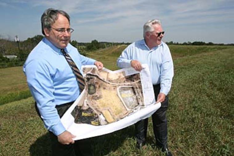 On the Gloucester County site, lawyer Robert W. Bucknam Jr. (left) and Bill Geary, president of Clean Harbors, hold plans for the solar array. (CHARLES FOX / Staff Photographer)