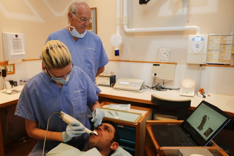 Center City dentist Dr. Peter Hunt looks at a computer screen while Chief Surgical Dental Assistant Silvy Bergler uses the Trios System on a model. The Trios System is a dental digital impression scanner. The same tool was used to make a mouthpiece for Eagles running back and punt returner Kenjon Barner.