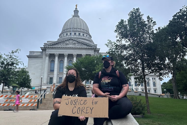 Lilly Nimmer, left, and Reba Bergmann, right, hold a sign to protest the police shooting of Corey Ruiz outside of the Wisconsin state Capitol during the weekly farmers market on Saturday, July 25, 2026, in Madison, Wisconsin.