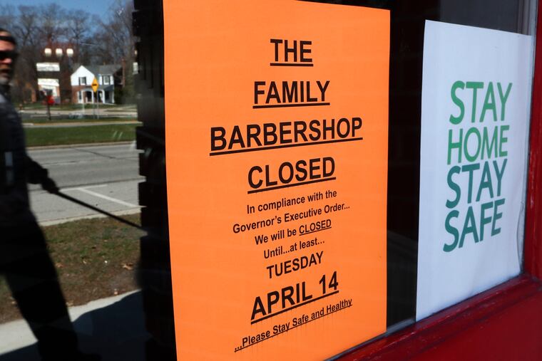 A pedestrian walks by The Family Barbershop, closed because of a Gov. Gretchen Whitmer executive order, in Grosse Pointe Woods, Mich.