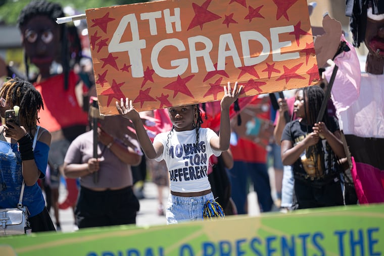 Blankenburg Elementary School fourth-grade student Maylyn Faison, 10, holds a sign up during the school's annual parade. The parade celebrates students' identities and causes they care about through giant puppets, original chants, drumming, and other artwork. Blankenburg is among 17 Philadelphia schools recently approved for closure by the school board.
