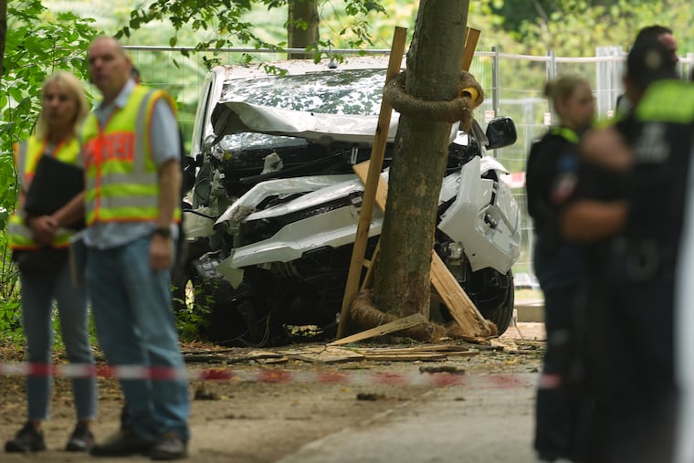 Police officers stand near a vehicle crashed into a tree after driving into a crowd near Berlin's annual Pride event, in Berlin, Germany, Sunday, July 26, 2026.