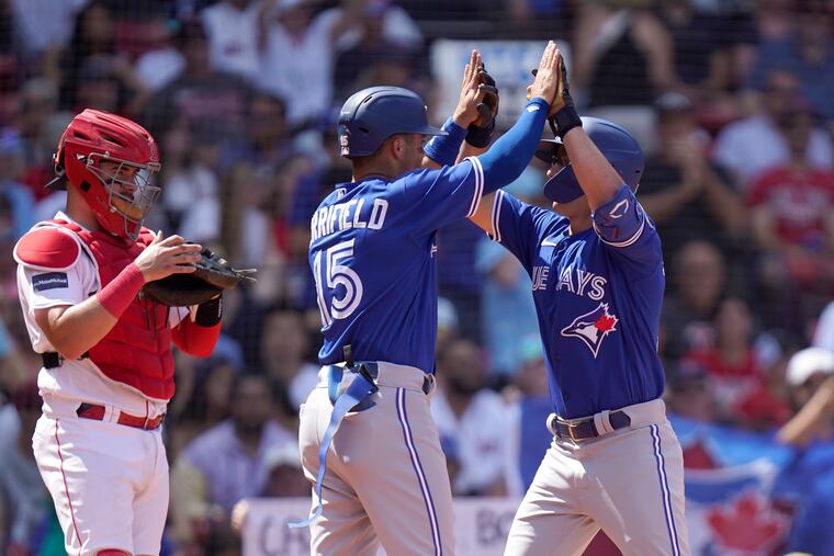 Toronto's Davis Schneider (right) celebrates his two-run homer on Sunday with Whit Merrifield as Boston Red Sox catcher Reese McGuire looks on.