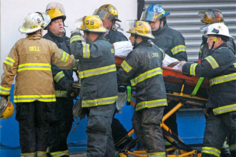 Holding the helmet of a fallen firefighter, a battalion chief (left) works along with rescue personnel to move the victim to a waiting medic unit at the fatal 5-alarm blaze in East Kensington. (Alejandro A. Alvarez / Staff Photographer)