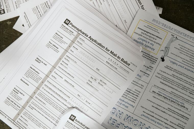 Absentee ballot applications in both Spanish and English along with fliers sit next to food boxes distributed by the city, school district, and non-profit groups at 401 Domino Lane in Roxborough on May 16. The goal of putting absentee ballot applications and fliers into the food boxes is to reach low-income voters who otherwise might not know about vote-by-mail, risking either not voting or voting in person.