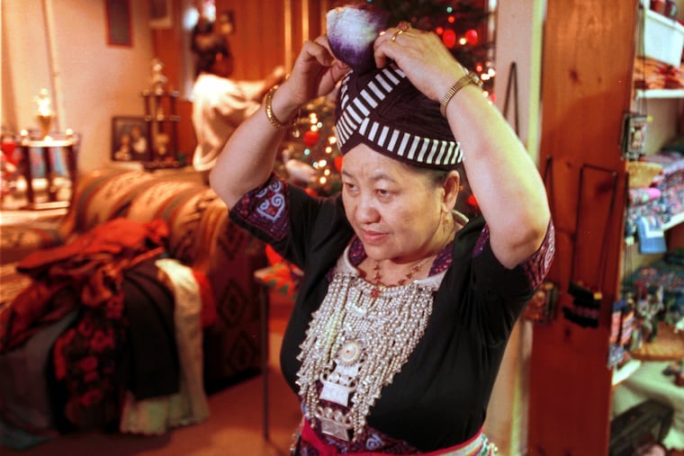 Pang Xiong Sirirathasuk Sikoun, in a 2000 photograph, uses a mirror to adjust her traditional Hmong outfit.