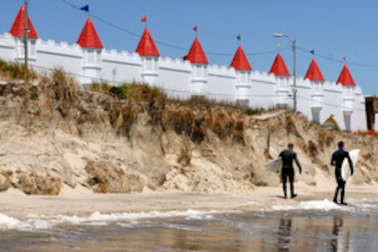 Surfers heading to a competition in Ocean City, N.J., pass a wall of sand that was a barrier dune before Monday's storm. Shore damage varied widely.