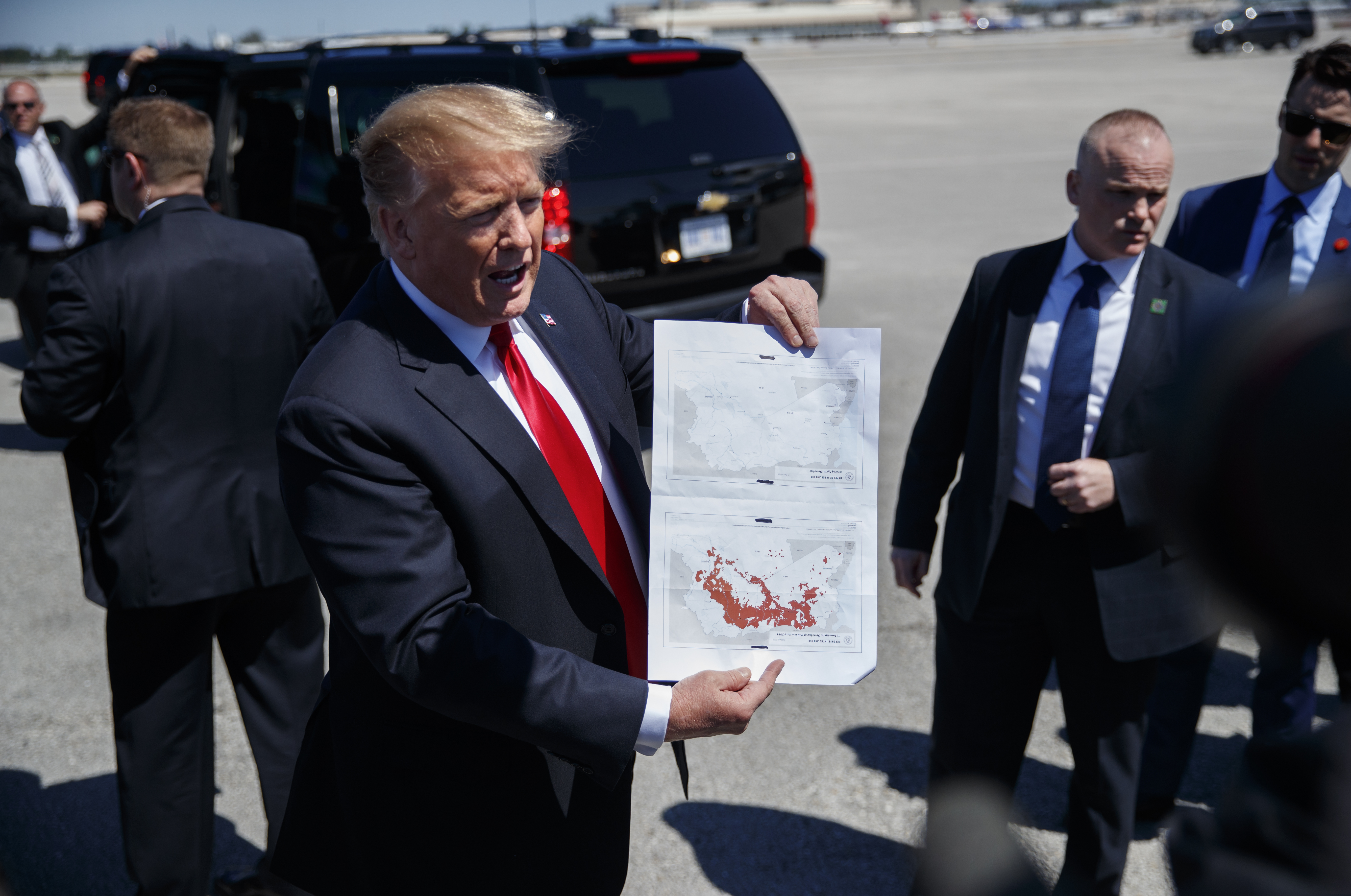 President Donald Trump holds a a copy of two maps of Syria as he arrives on Air Force One, Friday, March 22, 2019, at Palm Beach International Airport, in West Palm Beach, Fla. One map is awash in red shows IS controlled territory in Syria in November 2016. The other, without red, indicates that IS as of today no longer controls territory in Syria.