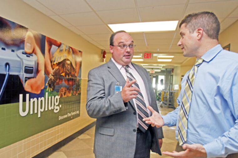 At Manor Elementary School in the Pennsbury District, principal Christopher Becker (right) and district Assistant Superintendent W. David Bowman talk in front of a large ad. (Akira Suwa / Staff Photographer)