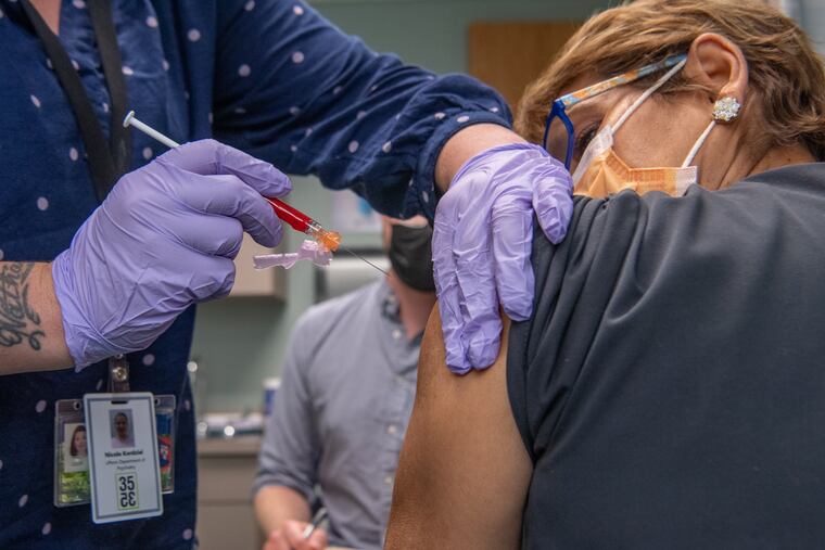 Nicole Kordziel, DNP, CRNP, gives Enelida Gomez, a nurse in Philadelphia, an investigational COVID-19 vaccine as part of the clinical trial for Moderna’s mRNA vaccine taking place at Penn Medicine. Seated in back, is William Vickroy, RN, BSN, a research nurse at Penn.