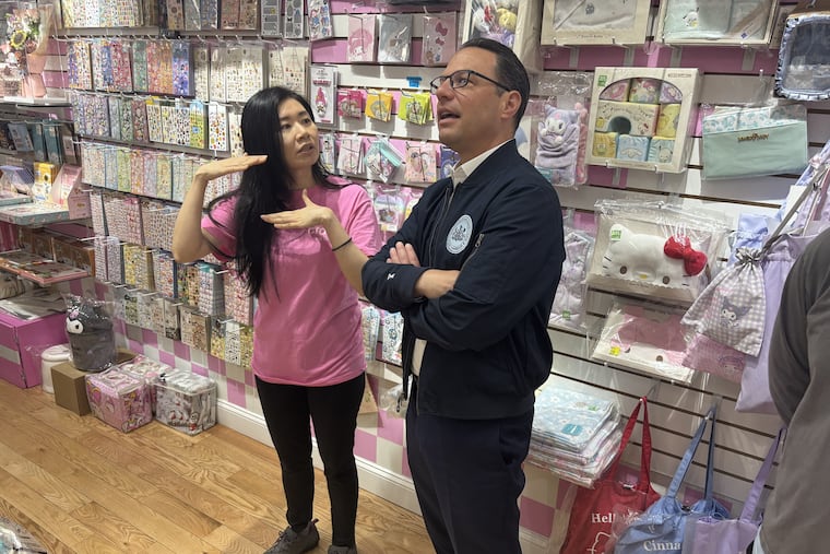 Debbie Law, owner of Asia Crafts, shows Gov. Josh Shapiro her merchandise at her Chinatown-based collectibles and gift shop on Wednesday.