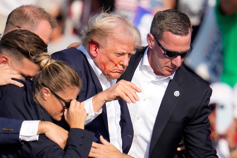Republican presidential candidate former President Donald Trump is helped off the stage at a campaign event in Butler, Pa., on Saturday, after a bullet grazed his right ear.