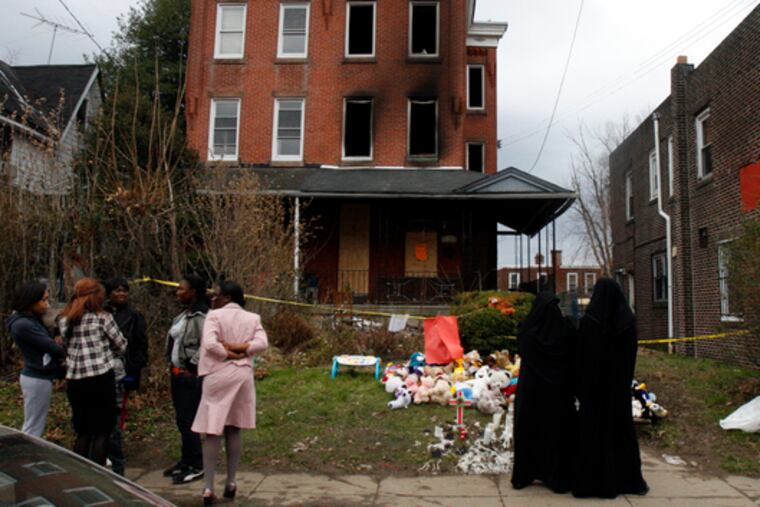 Neighbors mingle in front of the house in Southwest Philadelphia where seven people died in a fire Friday. Officials suspect a mishandled kerosene heater started the blaze.