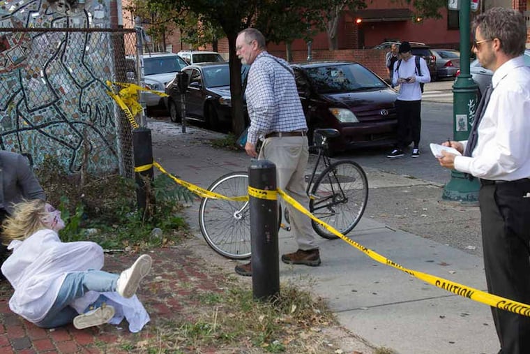 At left is Jesse Wellens pretending to be a detective as Jeana (no last name given ) made up to look like a zombie jumps out at unsuspecting pedestrians. Ed Bassmaster ( right) and his friends pull a prank along South St. near 11th on Friday, October 17, 2014. ( ALEJANDRO A. ALVAREZ / STAFF PHOTOGRAPHER )