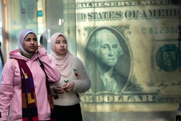 Egyptians walk past a poster depicting a U.S. dollar outside an exchange office in Cairo, Egypt. The value of the dollar is up more than 5% since the end of January.