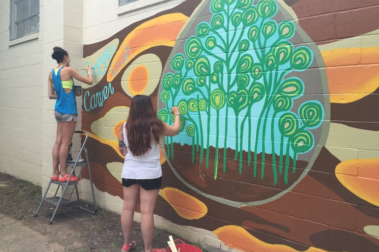 Alyssa Longobardi (left) and Alicia Qureshi work on a mural at the George Washington Carver Community Center in Norristown. The center and its pool will reopen Saturday. (JESSICA PARKS/Staff)